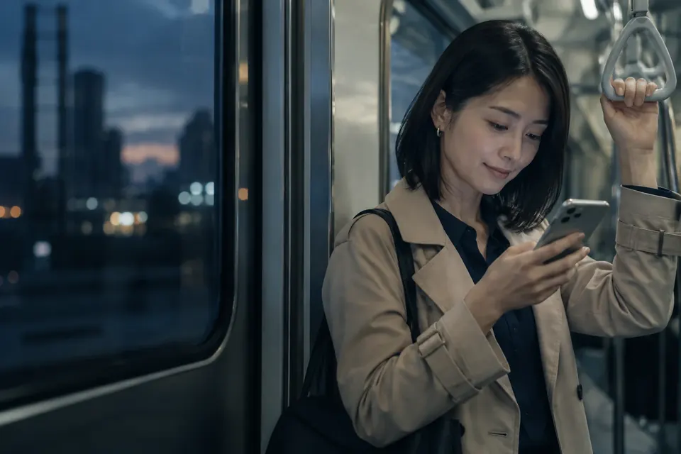 夕方の電車の中でスマートフォンにメッセージを打つ女性